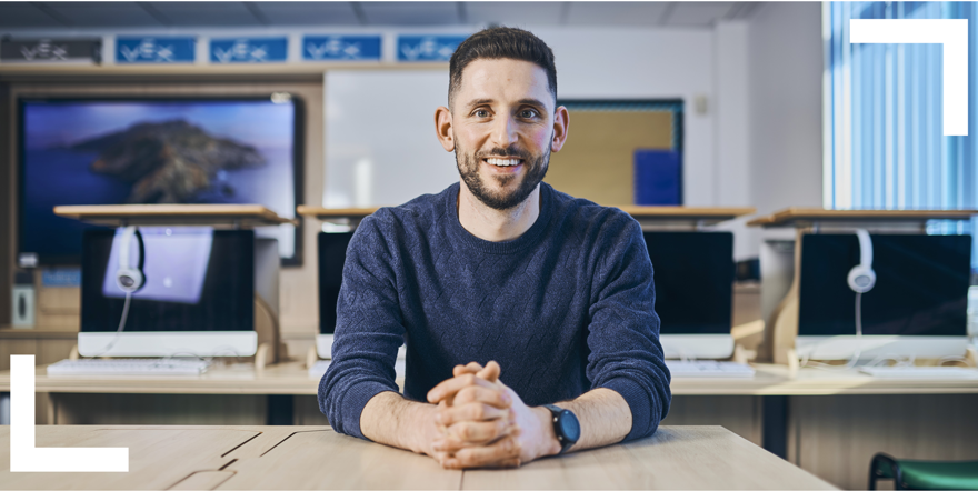 Friendly looking teacher sitting at classroom desk